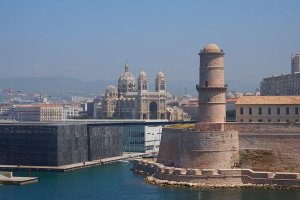 View of Marseille's Old Port entrance featuring the J4 building with the MuCEM museum, Villa Méditerranée, Sainte-Marie-Majeure Cathedral, and the pedestrian footbridge