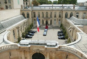 Top-down view of the Hôtel Matignon courtyard with black cars, a red carpet, and eight ceremonial guards at the entrance