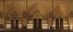 Lower front façade of Notre-Dame Cathedral in Paris showing three main portals and statues of 28 kings at night