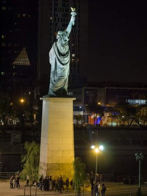 Nighttime view of Statue of Liberty replica illuminated against Paris skyline